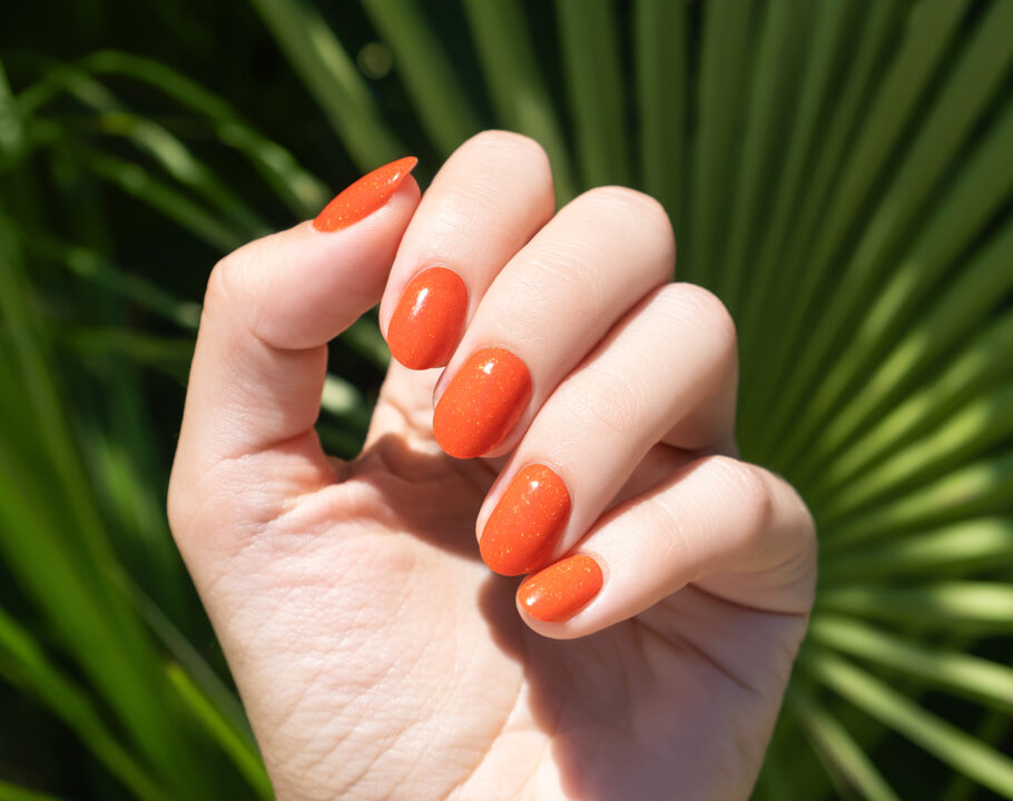 orange nail polish on hand-with palm tree background