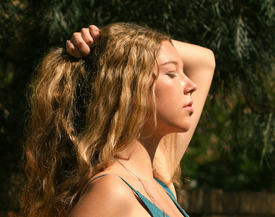 Woman holding up blonde wavy hair in the sunshine