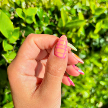 A close-up of a thumb nail with a neon pink and orange crocodile print.