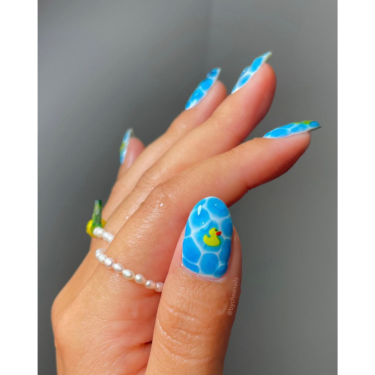 A close-up of a thumb nail with blue crocodile-themed manicure and nail art.