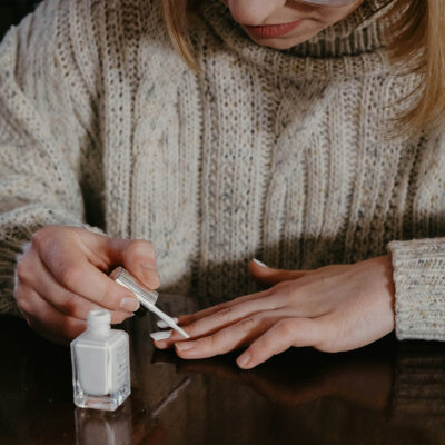 woman in a sweater painting her nails white