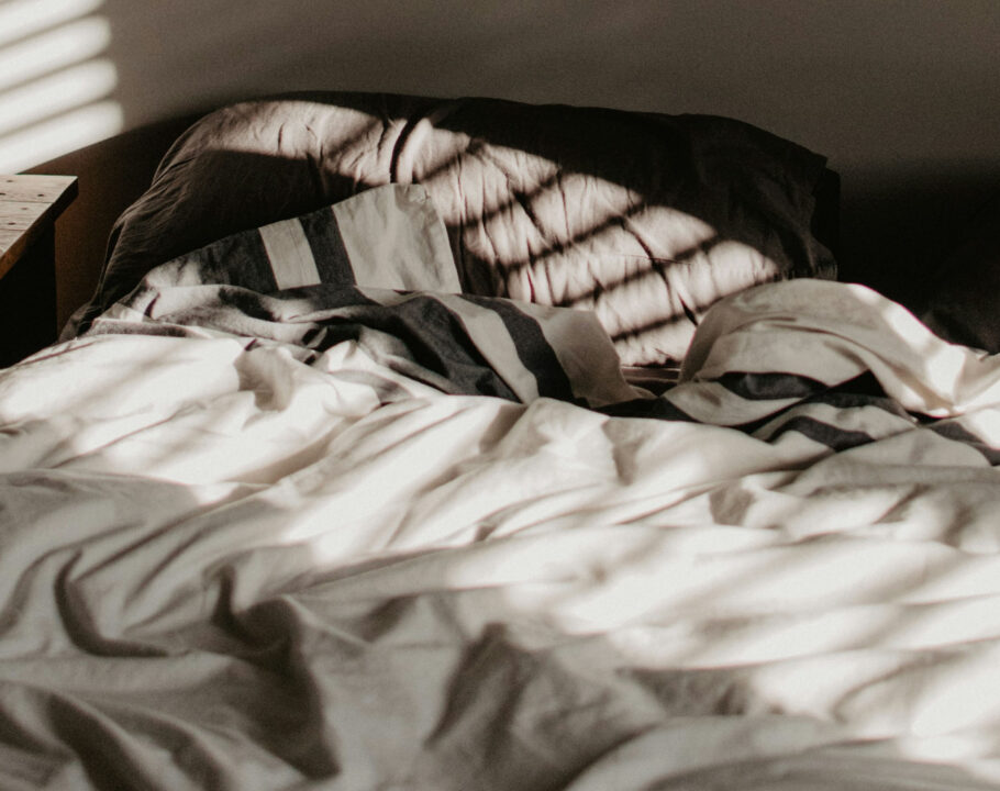 Empty bed in sunlit shadowed room with ruffled sheets