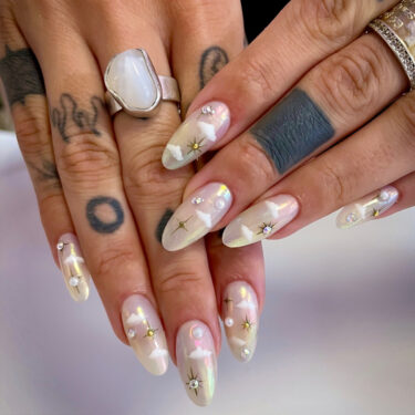 A close up of a woman's tattooed hands and her chrome cloud nails with emblems