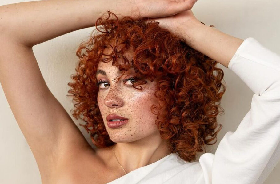 freckle-faced woman with short red curly hair and bangs