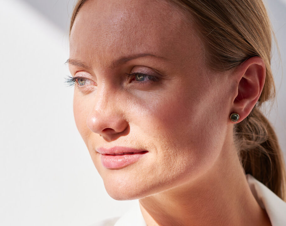 Adult modern woman in stylish white jacket looking pensively away on white background in bright sunlight